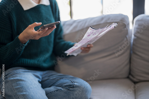 Schilderij op canvas Asian woman holding paper document calculating money savings paying bills in mobile application using smart phone payment online with paying household bills tax insurance managing budget