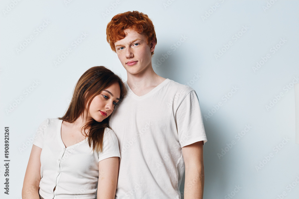 Naklejka premium Young couple standing close together on white background. Woman leaning head on man shoulder with casual white t shirts. Friendship, relationship and affection concept with studio portrait.