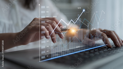 Obraz na płótnie A close-up of hands typing on a laptop with an overlay of digital financial graphs and metrics, ideal for illustrating business analysis and technology themes