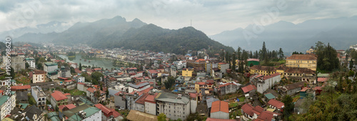 Aerial panorama of Sapa, Vietnam, showcasing its vibrant town, central lake, and surrounding misty mountains. A popular travel destination.