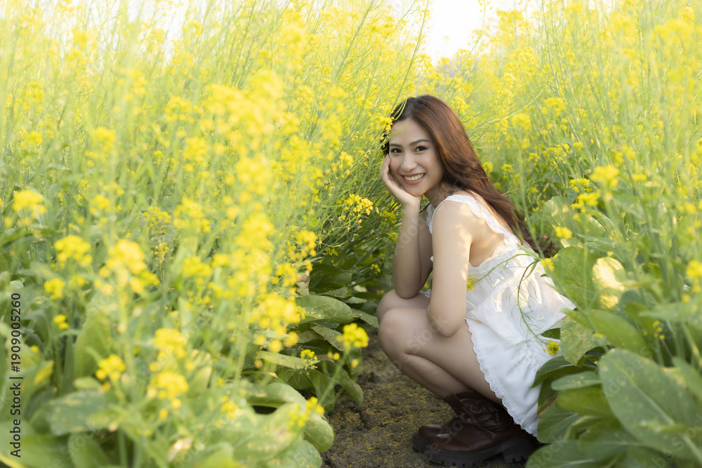 Fototapeta premium Happy young Asian woman smiling in beautiful yellow flower field. lovely lady in white dress enjoys serene outdoor summer day feeling joy and freedom