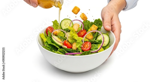 A person pours dressing over a fresh salad with lettuce cucumbers tomatoes croutons and red onions in a white bowl