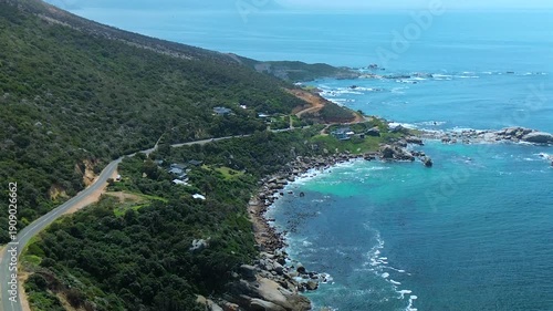 Professional cinematic shot of the rocky coastline and winding roads at the Cape of Good Hope, showing the Atlantic Ocean crashing against the arid South African shore.