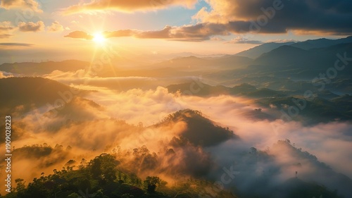 Mountains shrouded in mist at sunset, the sun shining softly through the clouds as it dips below the horizon