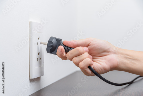 Wallpaper Mural Female hand inserting a black electrical plug into outlet Torontodigital.ca