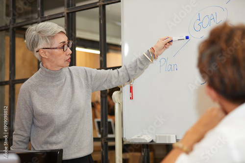 senior businesswoman writing on white board and talking to coworker in the office