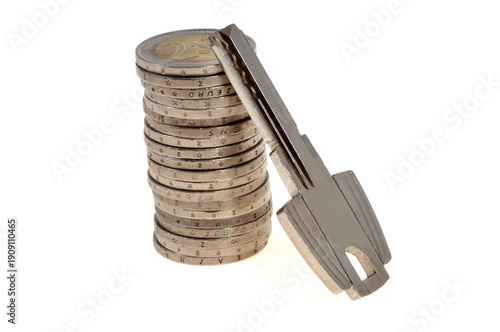 Concept de dépenses liées au logement avec une pile de pièces en euros et une clé de maison en gros plan isolées sur fond blanc