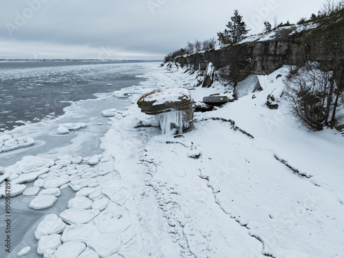 High angle drone view of Vaike-Pakri island rocky coast with limestone cliffs and frozen sea during winter in Estonia.