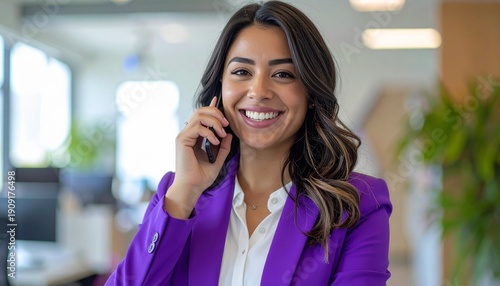 a smiling brunette woman with long hair wearing a purple blazer jacket making a telephone call in the office	