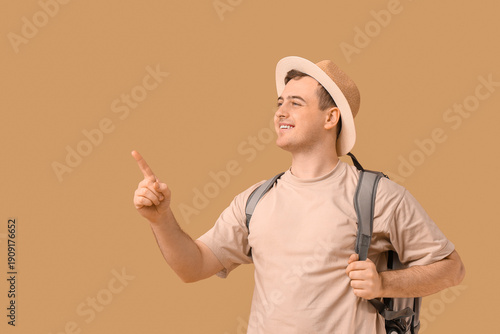 Young man with backpack pointing at something on brown background. Travel con...