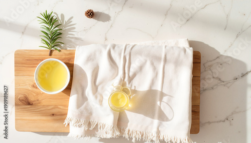 A textured linen towel with fringe lies on a bench, with cups of massage oil nearby