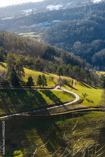 Winding mountain road curving through scenic green meadows and autumn forests in the Swiss Jura mountains near Waldenburg, Basel-Landschaft.