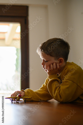 Wallpaper Mural Bored little boy sitting at table and playing with small toy airplane, daydreaming at home. Childhood, imagination and education concept Torontodigital.ca