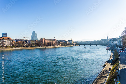 Obraz na płótnie Scenic view of the Rhine river in Basel, Switzerland, featuring historic brick architecture on the riverbank under a bright blue sky
