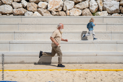 Energetic grandfather and young boy running up stone bleachers outdoors, showcasing intergenerational fitness, joy, and active lifestyle. Senior man and child exercising together in sunshine 