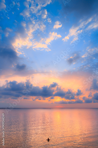 Relaxing by the sea at sunset. A man in the sea relaxes as he watches the sunset through the clouds.