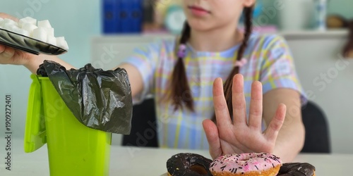 Wallpaper Mural A young girl gives up sugar while sitting at a table with colorful donuts and a trash can Torontodigital.ca
