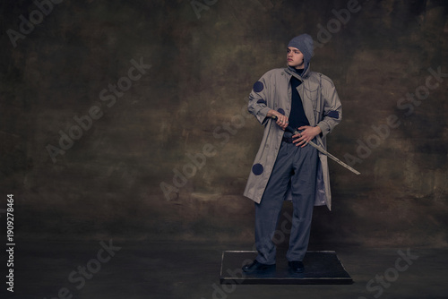 Fotografie Man in trench coat holding sword in dramatic studio scene