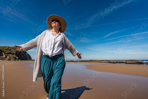 Beautiful middle-aged woman enjoying walk on sandy beach Monte Clerigo in Portugal on spring day. Front view