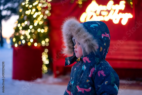 Warmly dressed child enjoying the festive sparkle of glowing holiday decorations