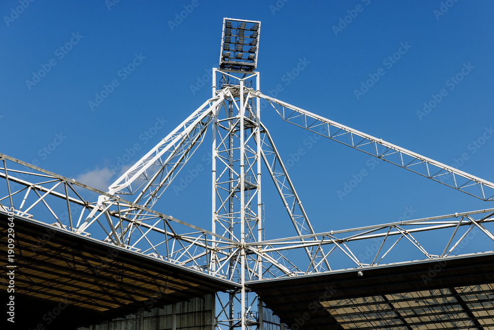 Fototapeta premium Metal stadium lighting tower with lamps and blue sky background