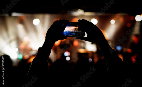 Hands holding smartphone recording live concert with crowd and stage lights