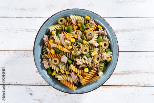 Pasta salad with tuna, corn and olives in bowl on white wooden table