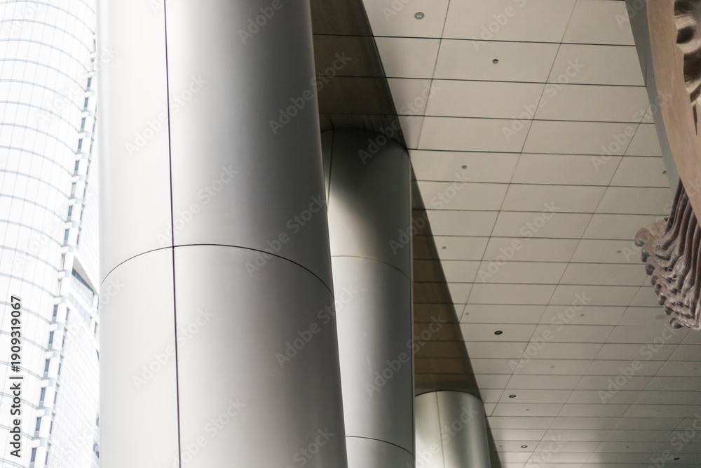 Obraz premium Several large steel columns rise to support a high ceiling inside a modern building. Natural light comes in through big glass windows nearby