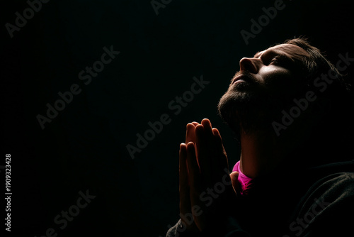 Young man praying in darkness with folded hands
