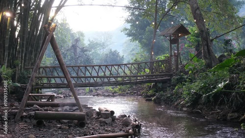 A woman walking across a wooden bridge with a canal flowing in the forest