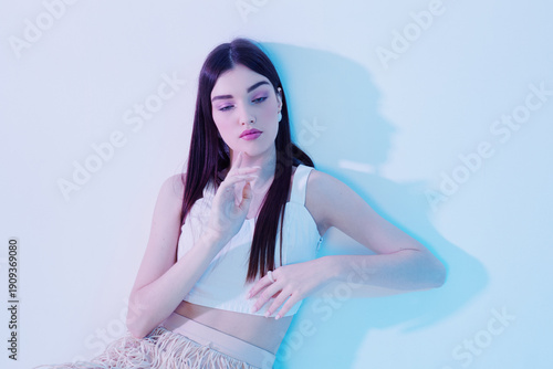 Foto Young woman with long dark hair poses in a white top against a light background