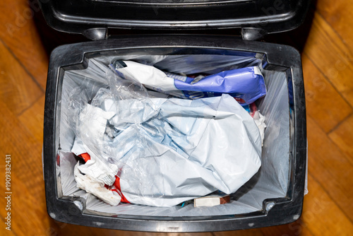 Trash bin filled with plastic packaging and household waste inside a kitchen. Overhead view photography. Household waste management and recycling concept.