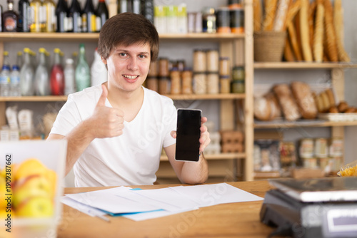 Принти на полотні Store manager behind the counter accepts the order and online payment through the app on the background of shelves with food