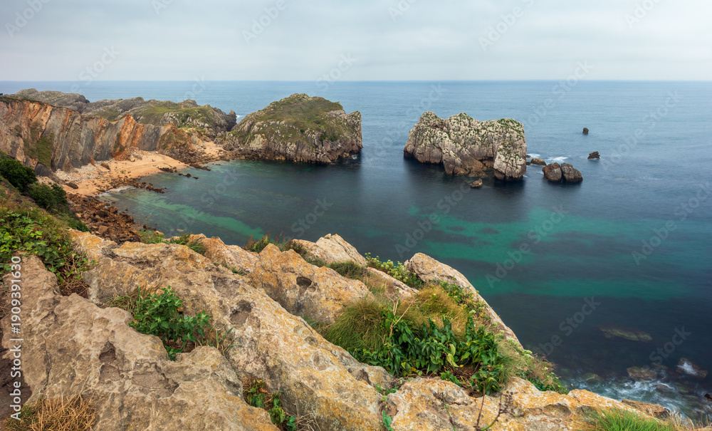 Fototapeta premium View of the sea with rock formations next to Somocuevas Beach, in the Costa Quebrada Geopark, Cantabria, Spain, on a cloudy summer day.