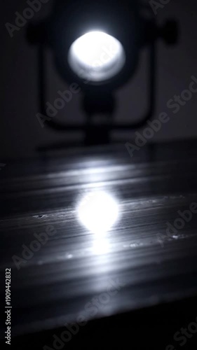 Bright spotlight illuminates a dark reflective surface with a strong reflection