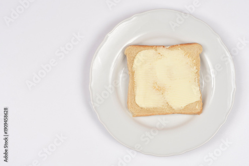 A single slice of crispy golden brown bread topped with a layer of creamy yellow butter served on a white ceramic plate against a plain white background