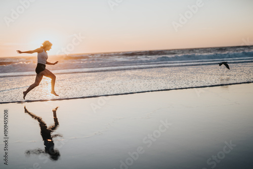 Fotografia A silhouette of a woman leaping along the shoreline at sunset, warm light and gentle waves create a dynamic, energetic mood ideal for fitness, travel, and lifestyle imagery