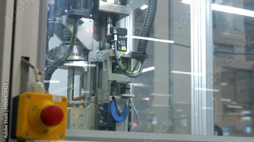 Precision robotic assembly machine in operation with emergency stop button and mechanical parts in a modern high tech industrial manufacturing factory environment