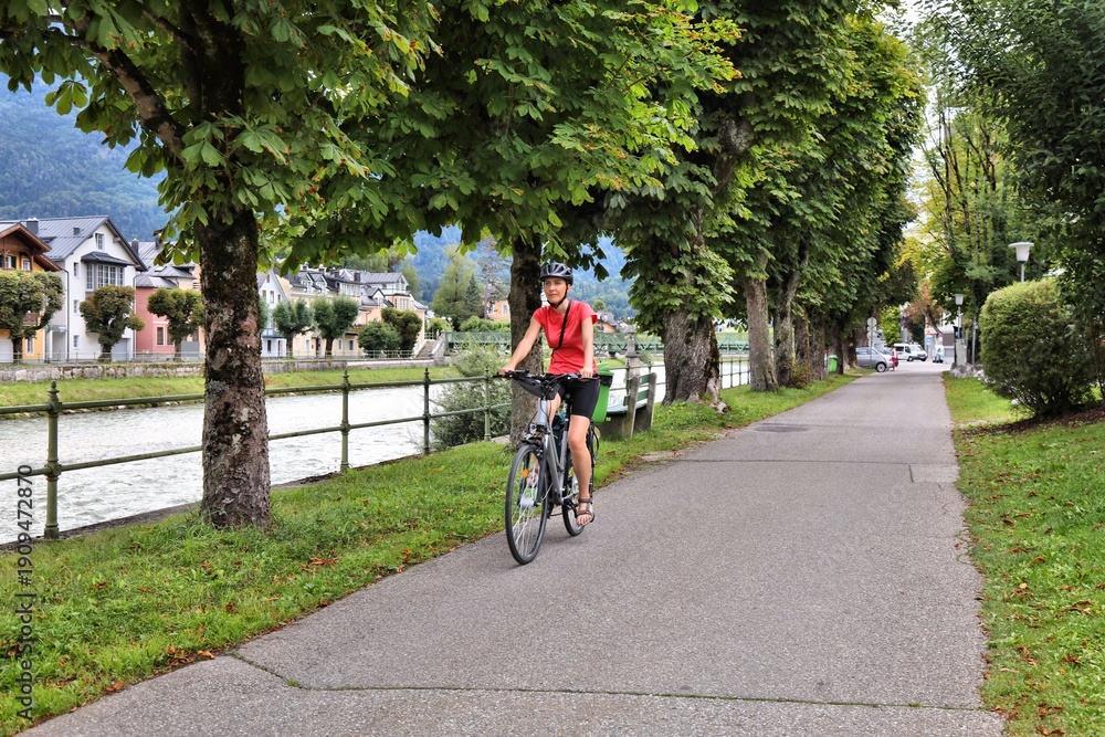 Naklejka premium Tourist on a bicycle along River Traun in Bad Ischl, Salzburg State, Austria. Woman cyclist on Salzkammergut Cycling Route (Salzkammergut-Radweg).