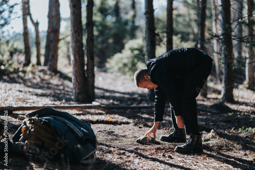 Cuadro en lienzo A man in black outdoor gear bends to touch a rock on a forest trail
