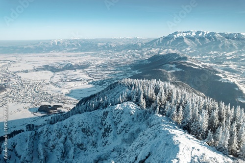 Obraz na plátně Snow-covered mountains rise against a clear blue sky, while a valley below sparkles with frost