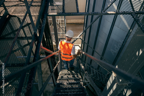 Φωτογραφία Senior male industrial worker wearing hard hat and orange vest descending metal