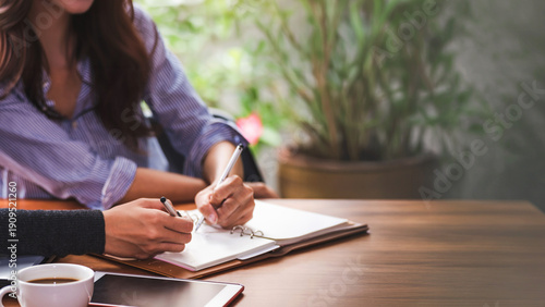 Hand of business people with pen and data sheet at meeting. Woman learning and reading a book together at coffee shop or cafe in the morning, vintage tone