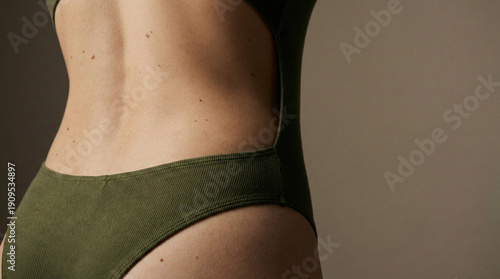 Close up of a woman back with natural moles wearing a textured olive green swimsuit