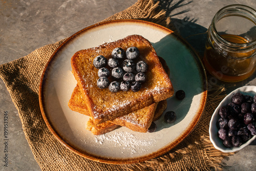 Fotografie Delicious homemade French toast topped with fresh blueberries and powdered sugar, served with honey and flowers on a rustic table