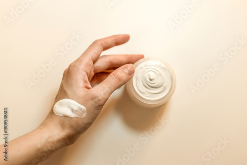 Hand, face or body cream. A woman's hand holding a mock-up of a white glass jar with cream on a light background. The concept of cosmetics, skin care, nutrition and hydration.