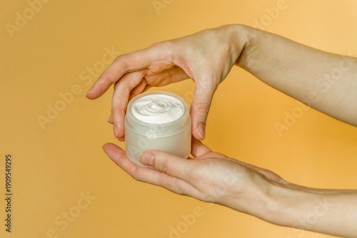 Hand, face or body cream. A woman's hand holding a mock-up of a white glass jar with cream on a light background. The concept of cosmetics, skin care, nutrition and hydration.