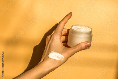Hand, face or body cream. A woman's hand holding a mock-up of a white glass jar with cream on a light background. The concept of cosmetics, skin care, nutrition and hydration.