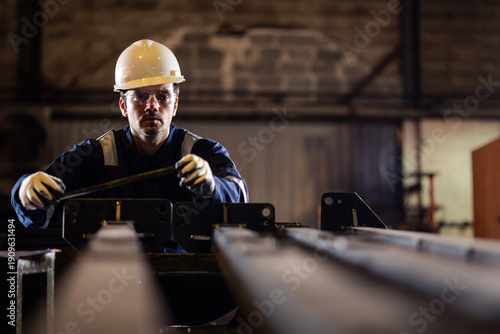 Photography Industrial worker measuring a metal component in a factory workshop while wearing safety helmet and gloves, ensuring precision, quality control, and workplace safety in manufacturing process