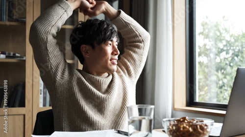 Wallpaper Mural Man stretches, smiling, at a desk with laptop, window, snack, and water Torontodigital.ca